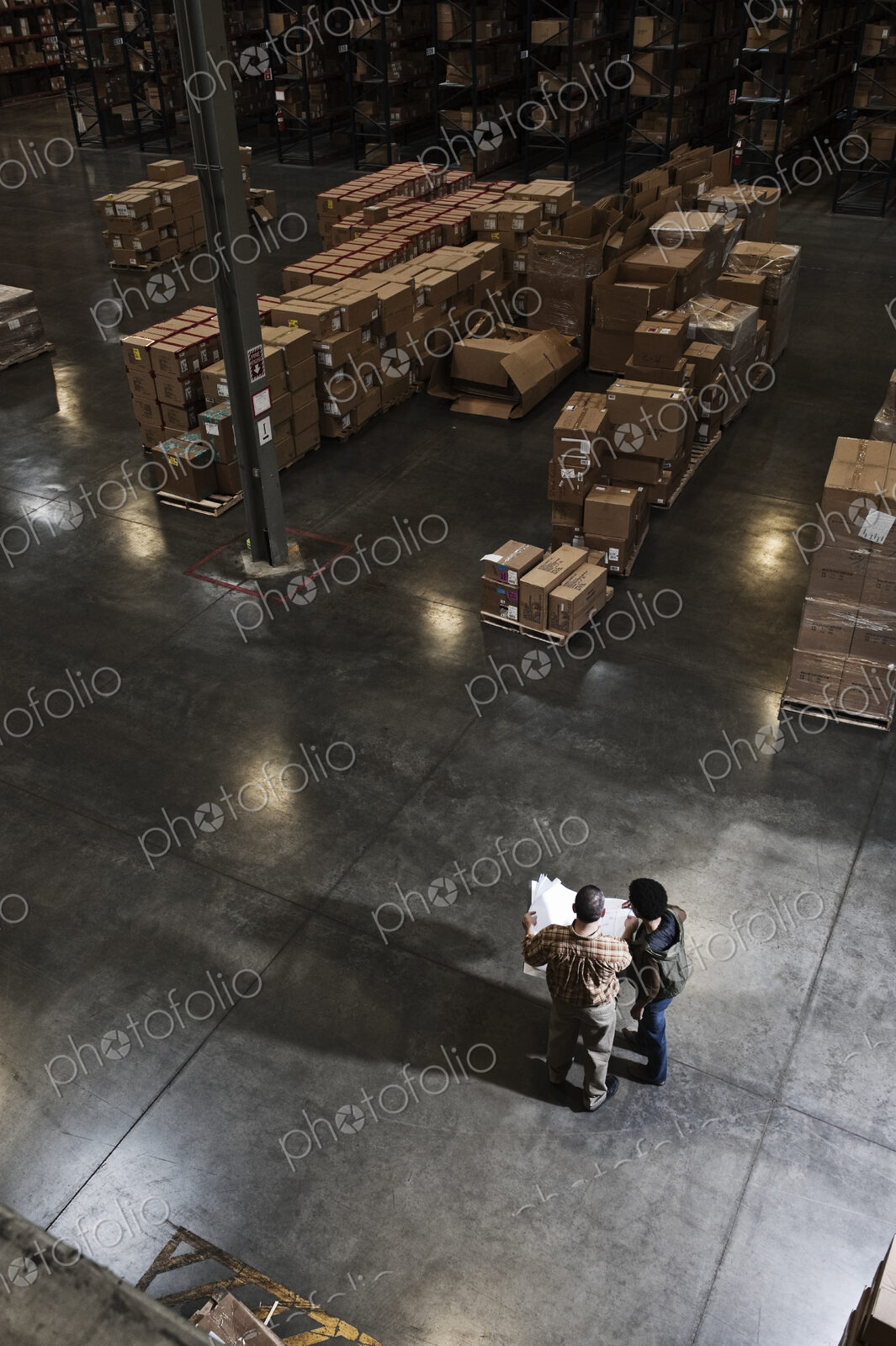 Two warehouse workers going over inventory sheets of products in a distribution warehouse.