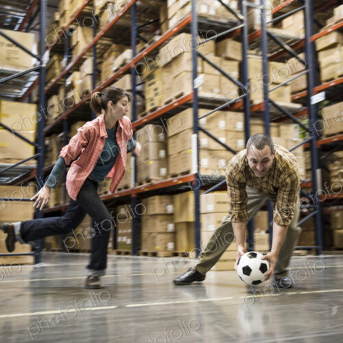 Two warehouse workers playing soccer during a work break in a distribution warehouse. Two warehouse workers playing soccer during a work break in a distribution warehouse.