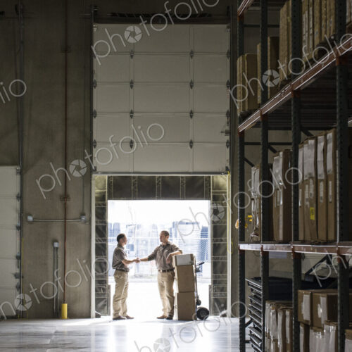 Two warehouseworkers shaking hands in the door of a loading dock in a warehouse. Two warehouseworkers shaking hands in the door of a loading dock in a warehouse.