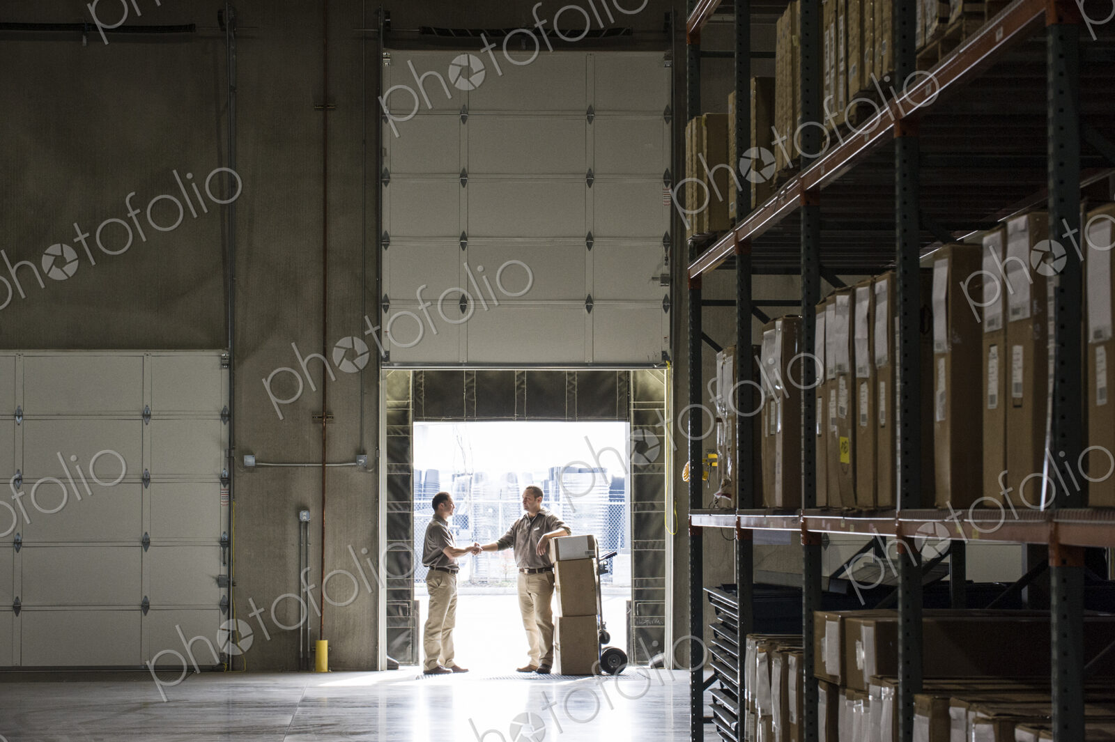 Two warehouseworkers shaking hands in the door of a loading dock in a warehouse.