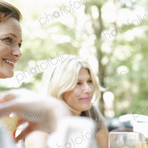 Two woman sitting at a table side by side in a garden. Talking and laughing. Two woman sitting at a table side by side in a garden. Talking and laughing.