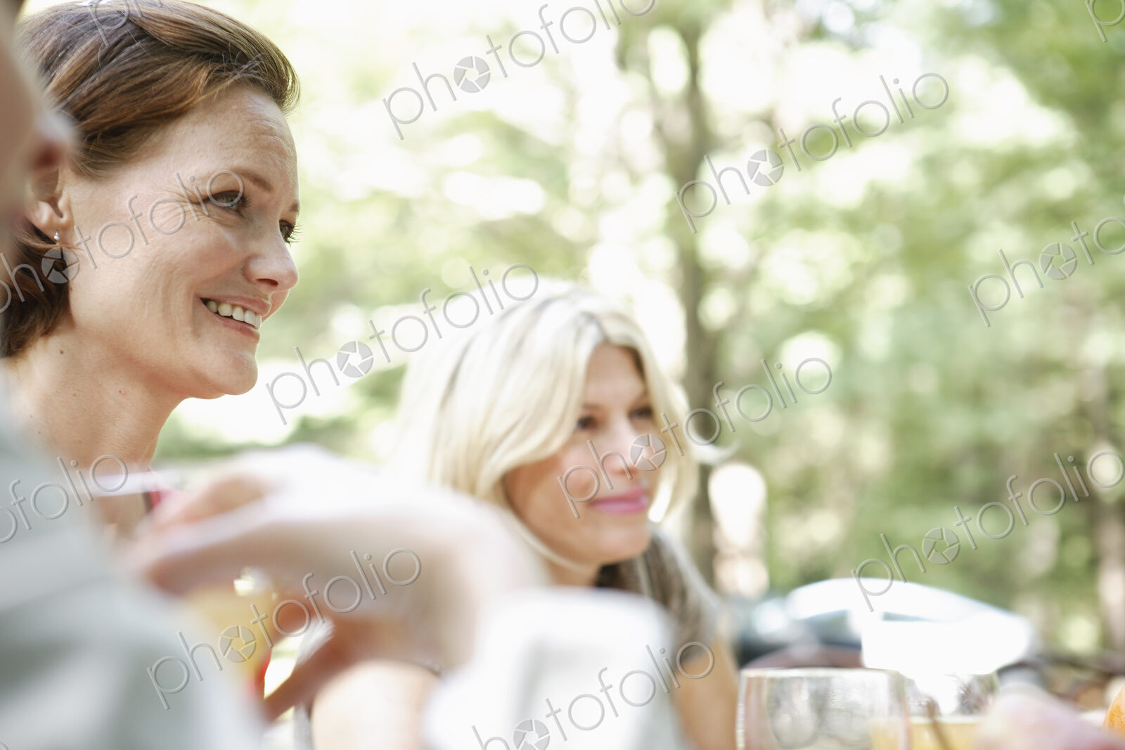 Two woman sitting at a table side by side in a garden. Talking and laughing.