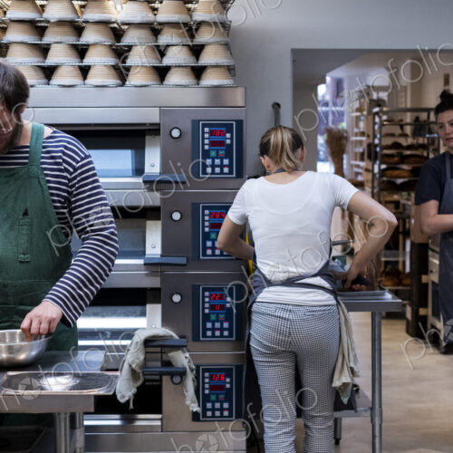 Two women and a man wearing aprons working in an artisan bakery.