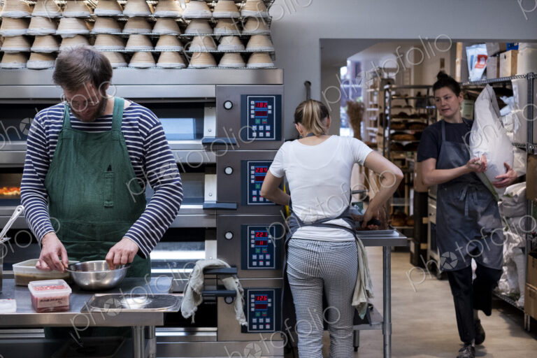 Two women and a man wearing aprons working in an artisan bakery.