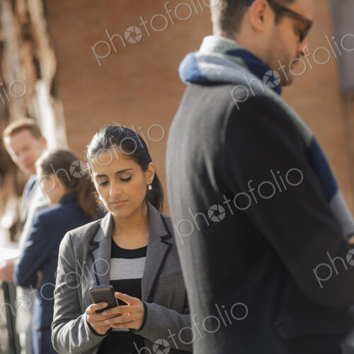 Two women and two men on the sidewalk. Two people checking their mobile phones. Two women and two men on the sidewalk. Two people checking their mobile phones.