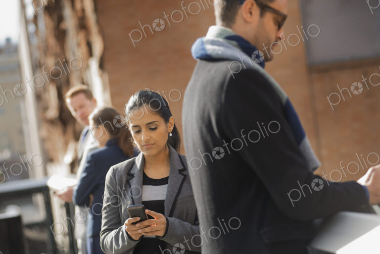 Two women and two men on the sidewalk. Two people checking their mobile phones.