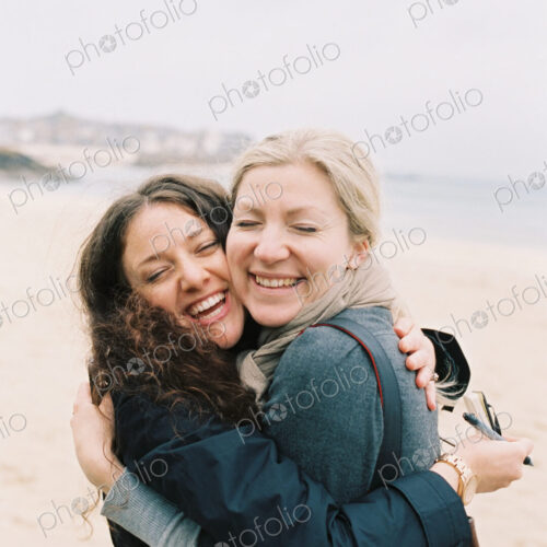 Two women cheek to cheek hugging on a beach. Two women cheek to cheek hugging on a beach.