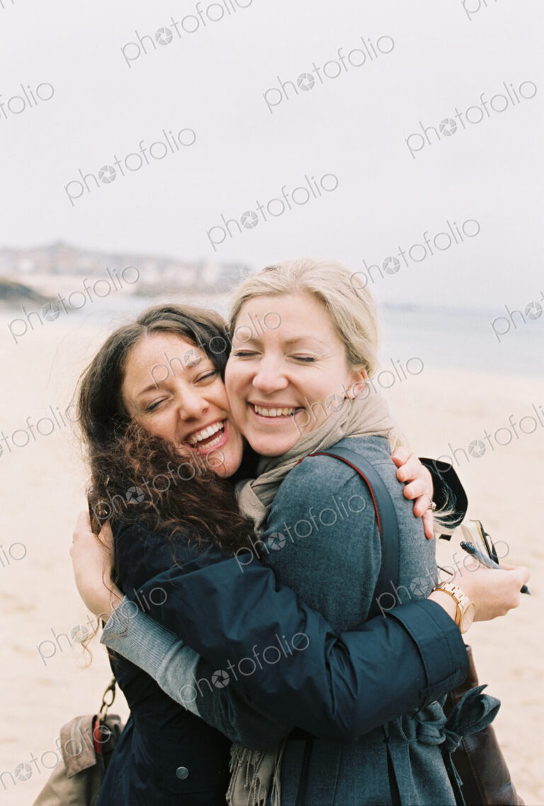 Two women cheek to cheek hugging on a beach.