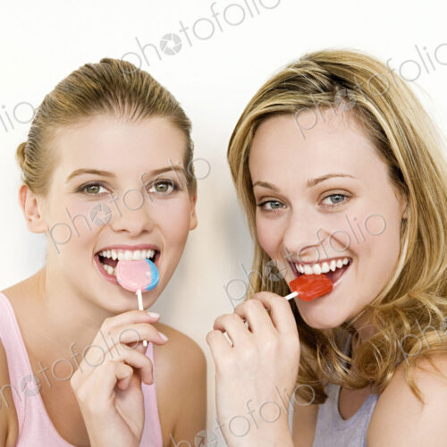 Two women eating lollipops and looking at the camera.