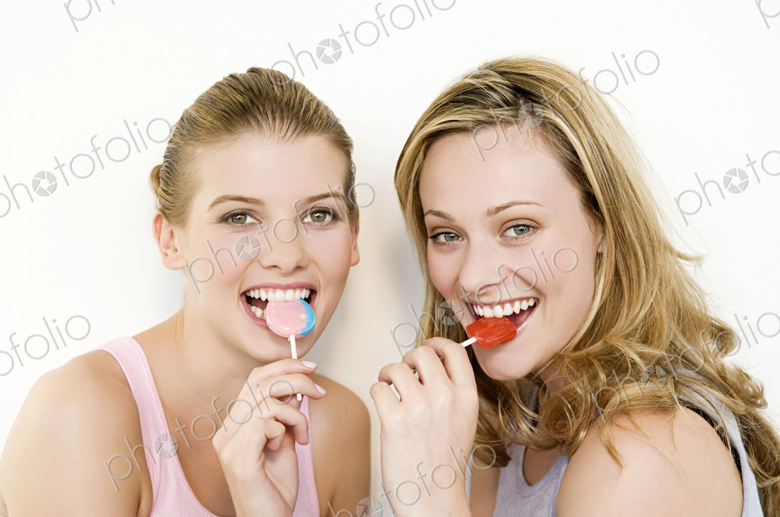 Two women eating lollipops and looking at the camera.