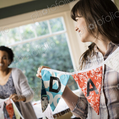 Two women hanging up bunting with lettering, decorating for a party. Two women hanging up bunting with lettering, decorating for a party.