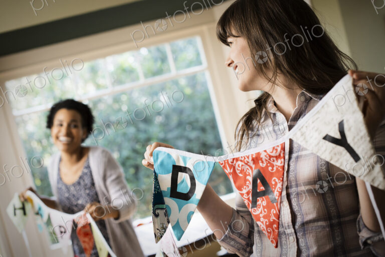Two women hanging up bunting with lettering, decorating for a party.