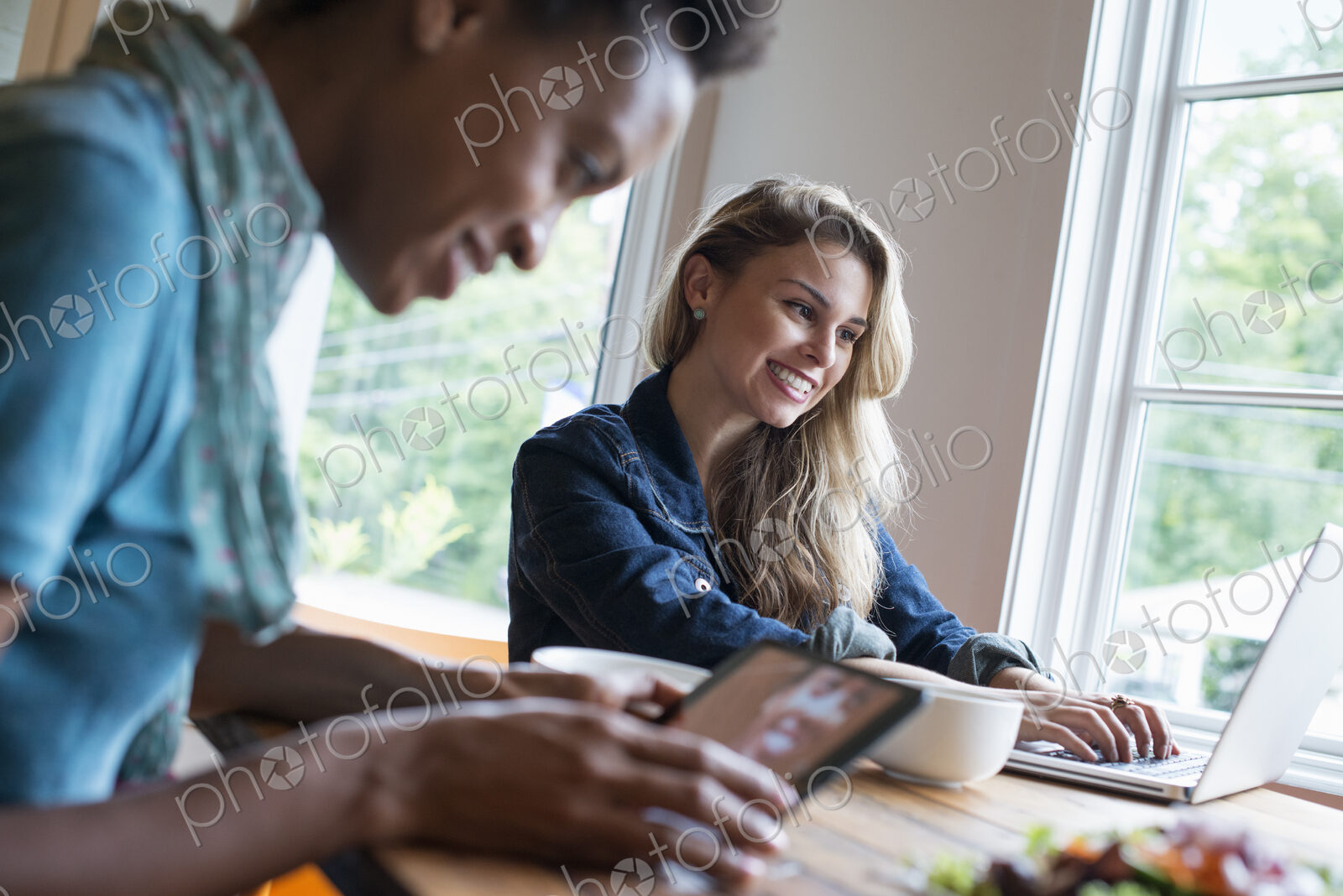 Two women in a cafe. Using a digital tablet and laptop. Working and keeping in touch.