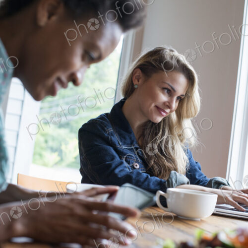 Two women in a cafe. Using a digital tablet and laptop. Working and keeping in touch. Two women in a cafe. Using a digital tablet and laptop. Working and keeping in touch.