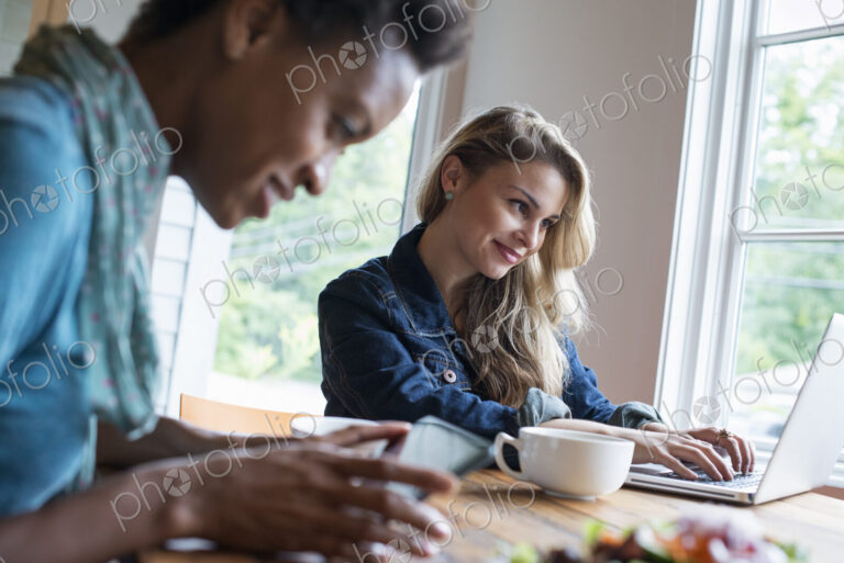 Two women in a cafe. Using a digital tablet and laptop. Working and keeping in touch.