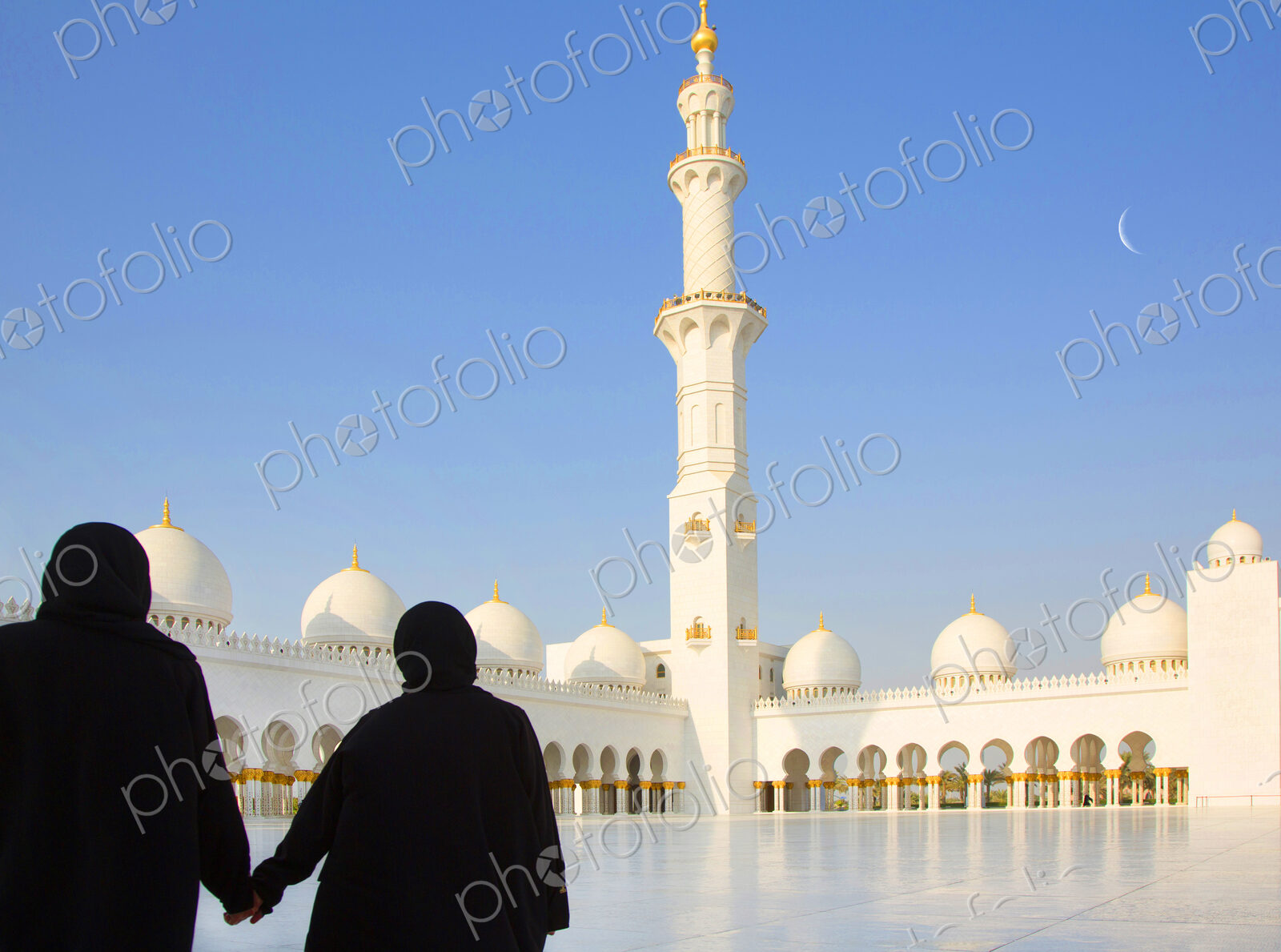 Two women in a mosque courtyard of colonnades, minaret and domes.