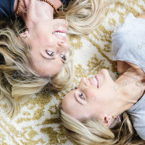 Two women lying on their backs looking at each other and laughing.
