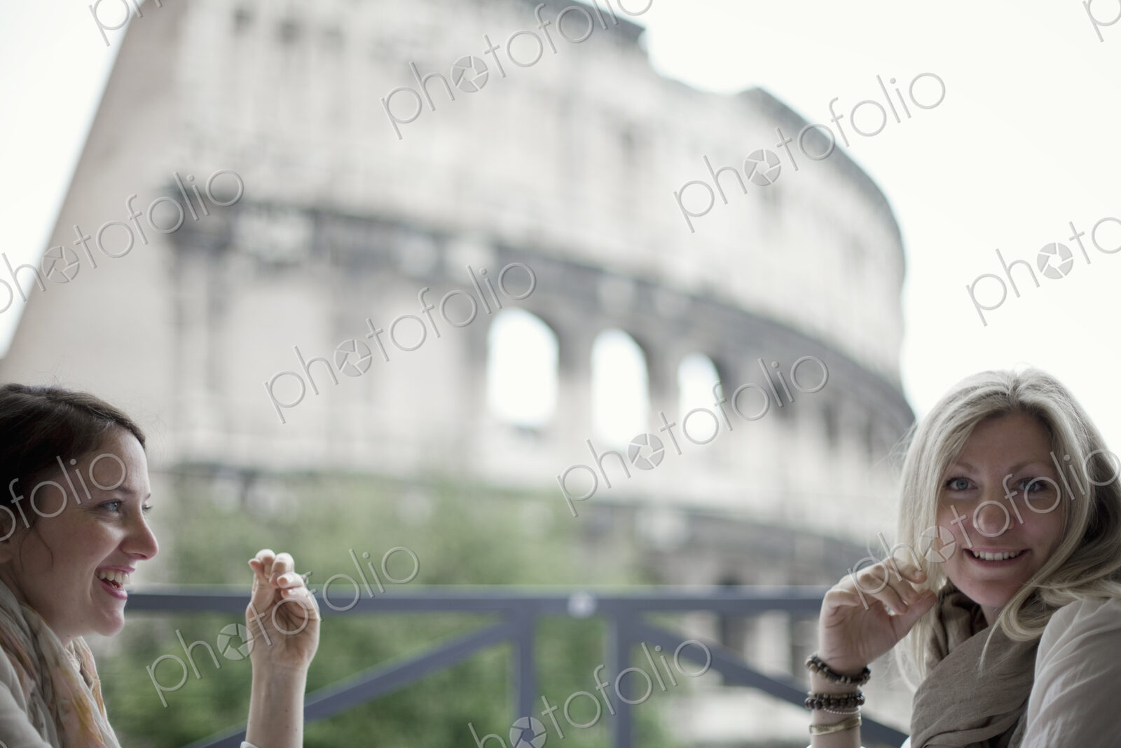 Two women seated on a terrace overlooking the huge Roman amphitheatre building, the…