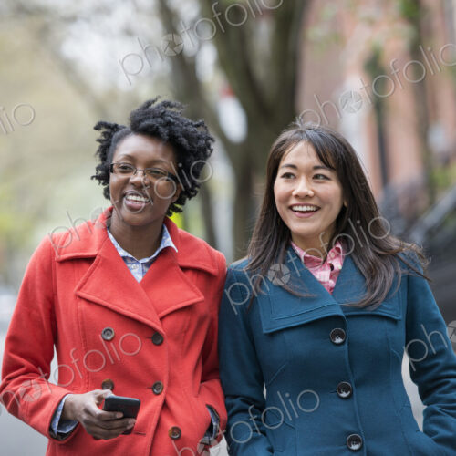 Two women side by side on a city street. One holding a cell phone.