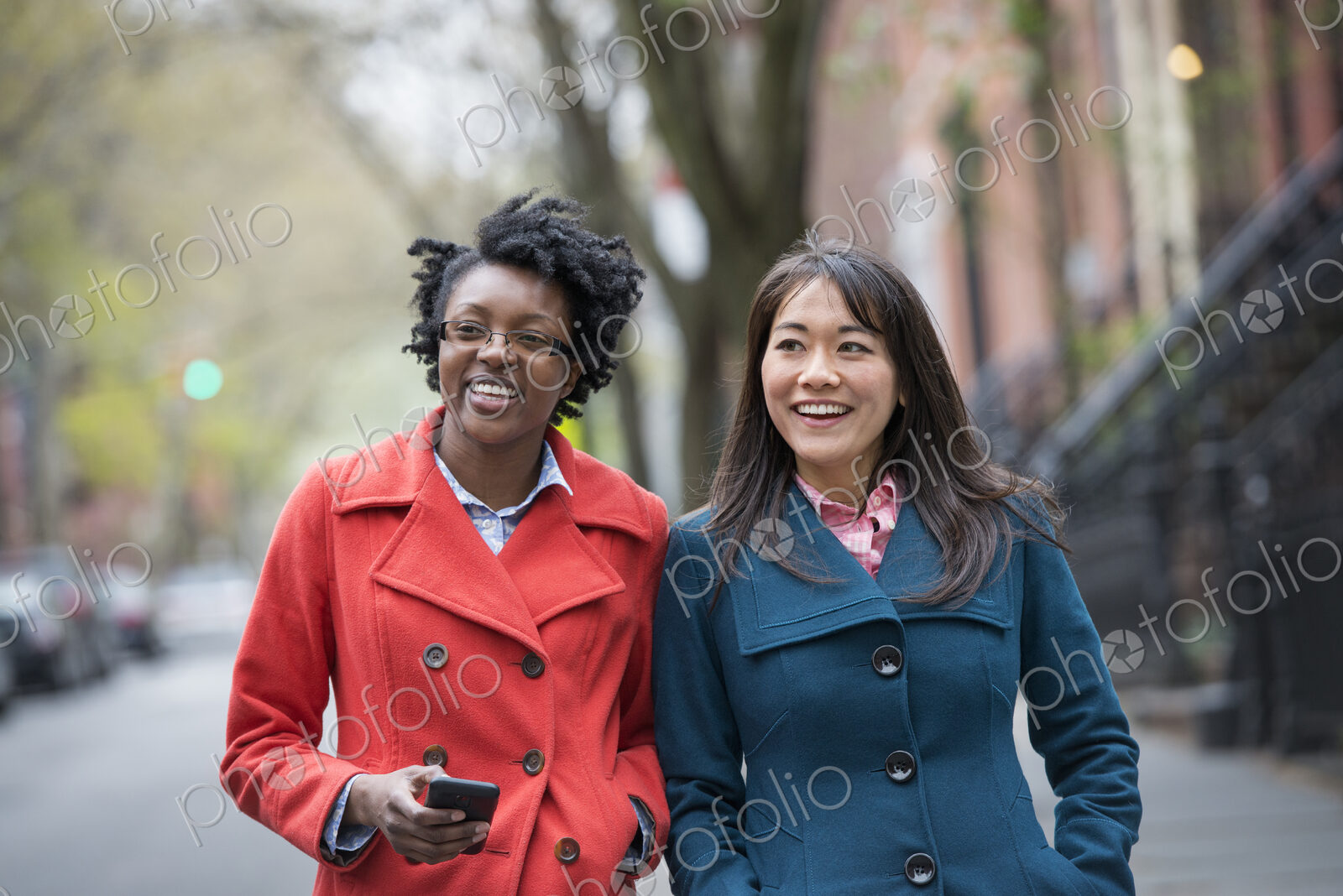 Two women side by side on a city street. One holding a cell phone.