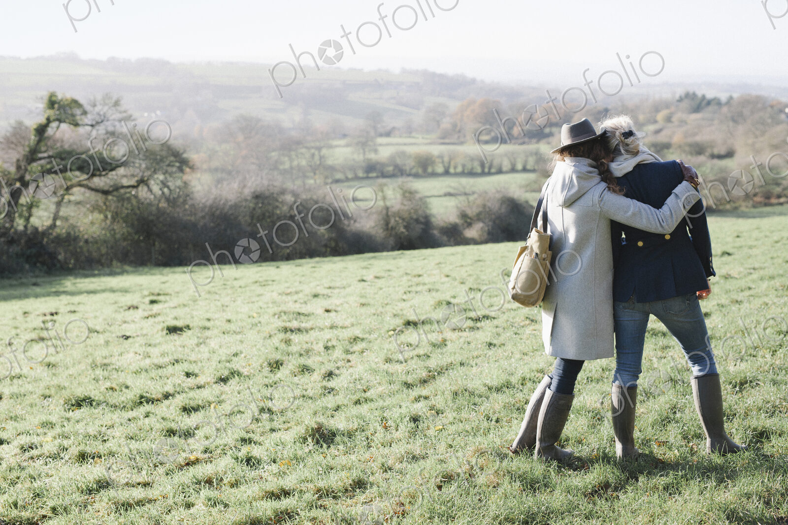 Two women side by side on a grass slope overlooking the landscape of Dorset.