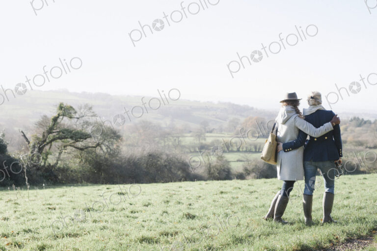 Two women side by side on a grass slope overlooking the landscape of Dorset.