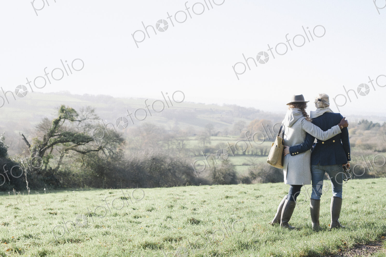 Two women side by side on a grass slope overlooking the landscape of Dorset.