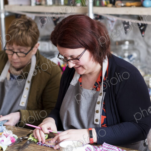 Two women sitting at a table in a workshop, making fabric flowers.