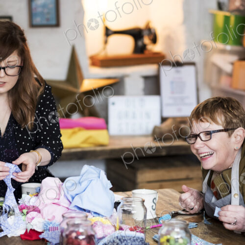 Two women sitting at a table in a workshop, making fabric flowers.