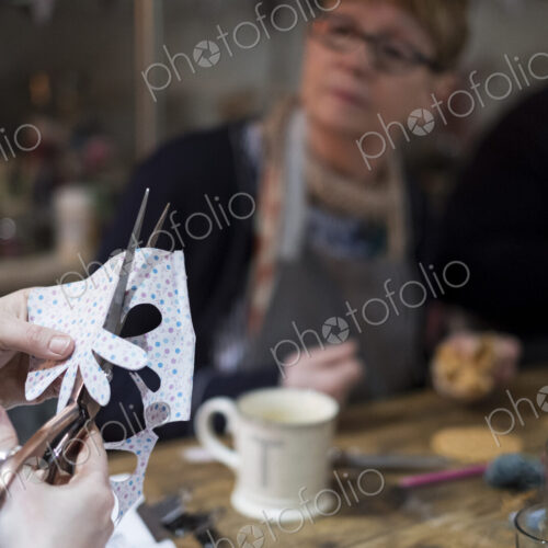 Two women sitting at a table in a workshop, making fabric flowers.