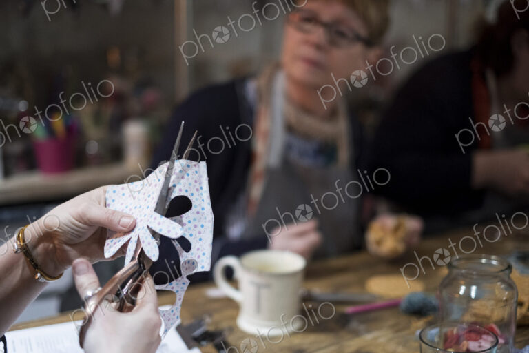 Two women sitting at a table in a workshop, making fabric flowers.