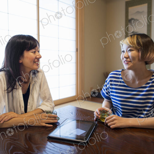 Two women sitting at a table with a digital tablet.