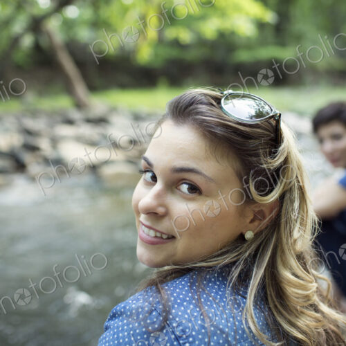 Two women sitting by a river bank looking over their shoulders.