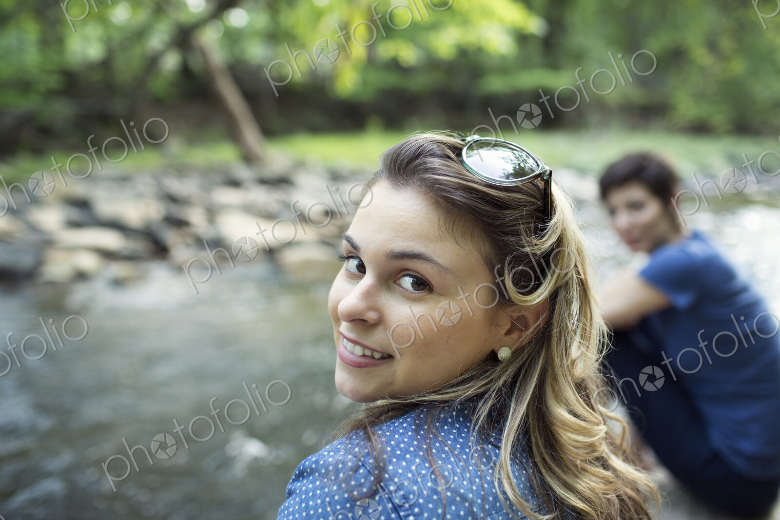 Two women sitting by a river bank looking over their shoulders.