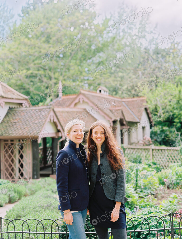 Two women standing in a garden of a historic house.