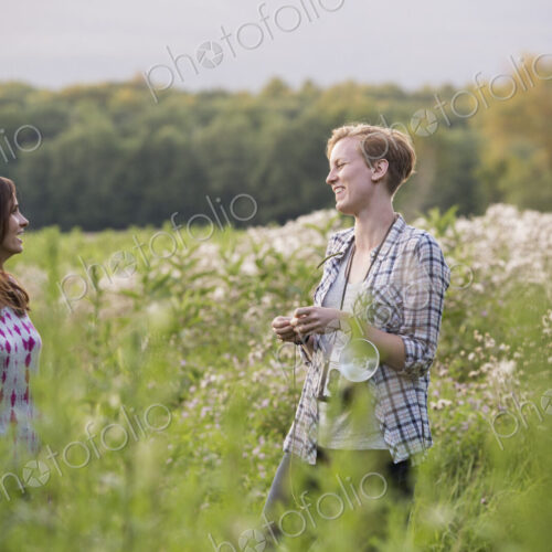 Two women standing in a meadow surrounded by tall grass and wild flowers. Two women standing in a meadow surrounded by tall grass and wild flowers.