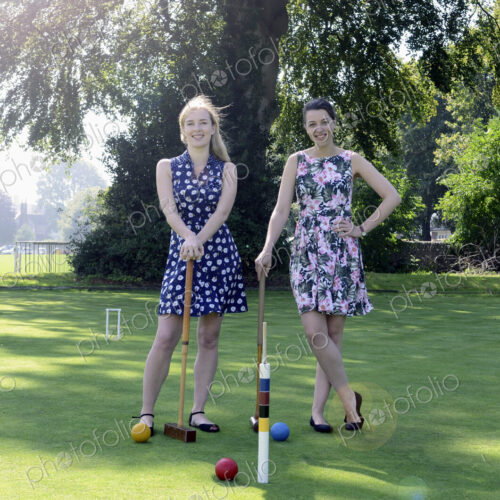Two women standing on croquet field with mallets and balls, smiling at camera.