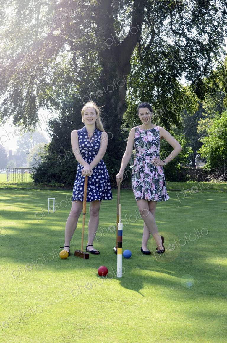 Two women standing on croquet field with mallets and balls, smiling at camera.