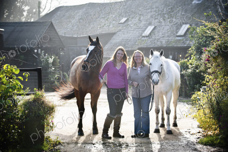 Two women standing outside a stable with two horses.