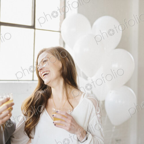 Two women standing side by side holding drinks. White balloons, party decorations. Two women standing side by side holding drinks. White balloons, party decorations.