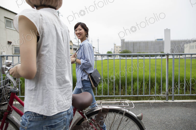 Two women walking along a footpath, pushing a bicycle.