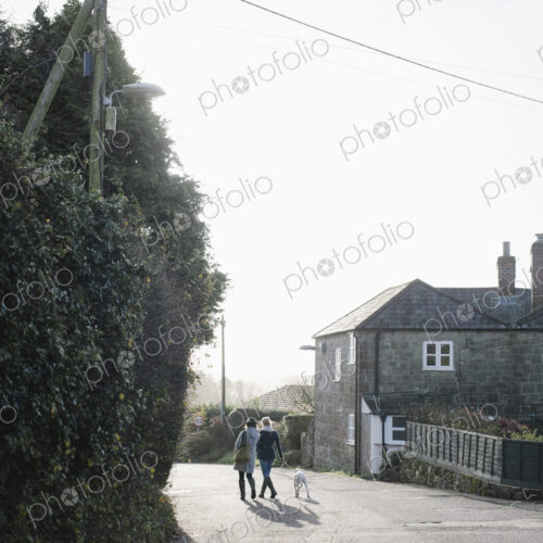 Two women walking along a village street with a dog on a lead. Two women walking along a village street with a dog on a lead.