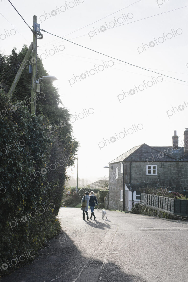 Two women walking along a village street with a dog on a lead.