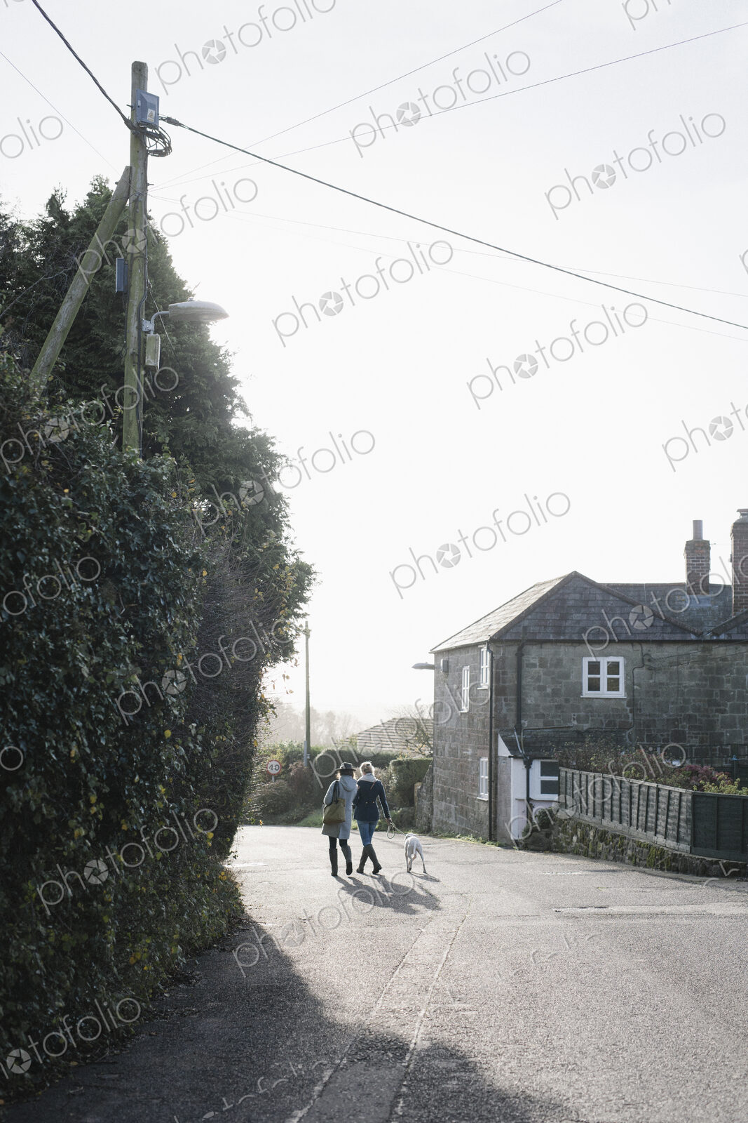 Two women walking along a village street with a dog on a lead.