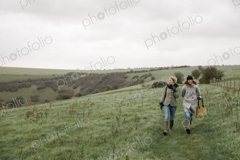 Two women walking on a country path across grassland.