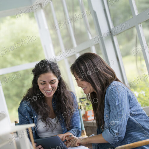 Two women working together, looking at the screen of a digital tablet.
