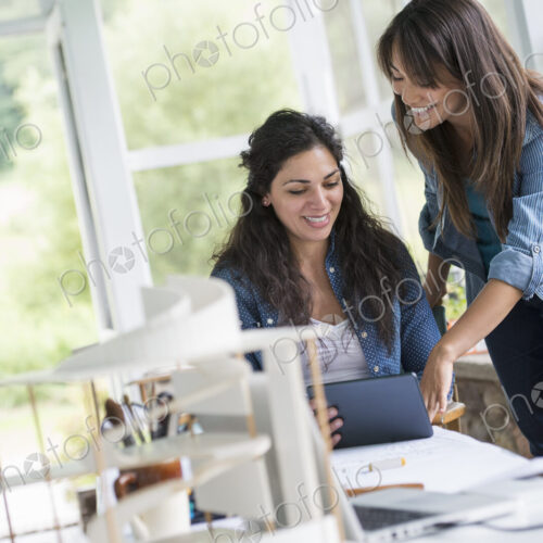 Two women working together, looking at the screen of a digital tablet. Two women working together, looking at the screen of a digital tablet.