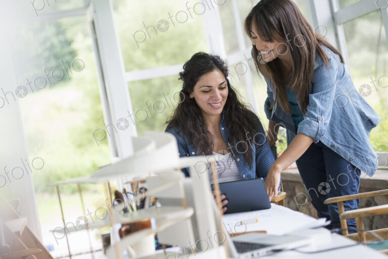 Two women working together, looking at the screen of a digital tablet.