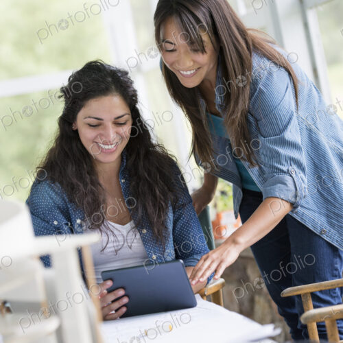 Two women working together, looking at the screen of a digital tablet. Two women working together, looking at the screen of a digital tablet.