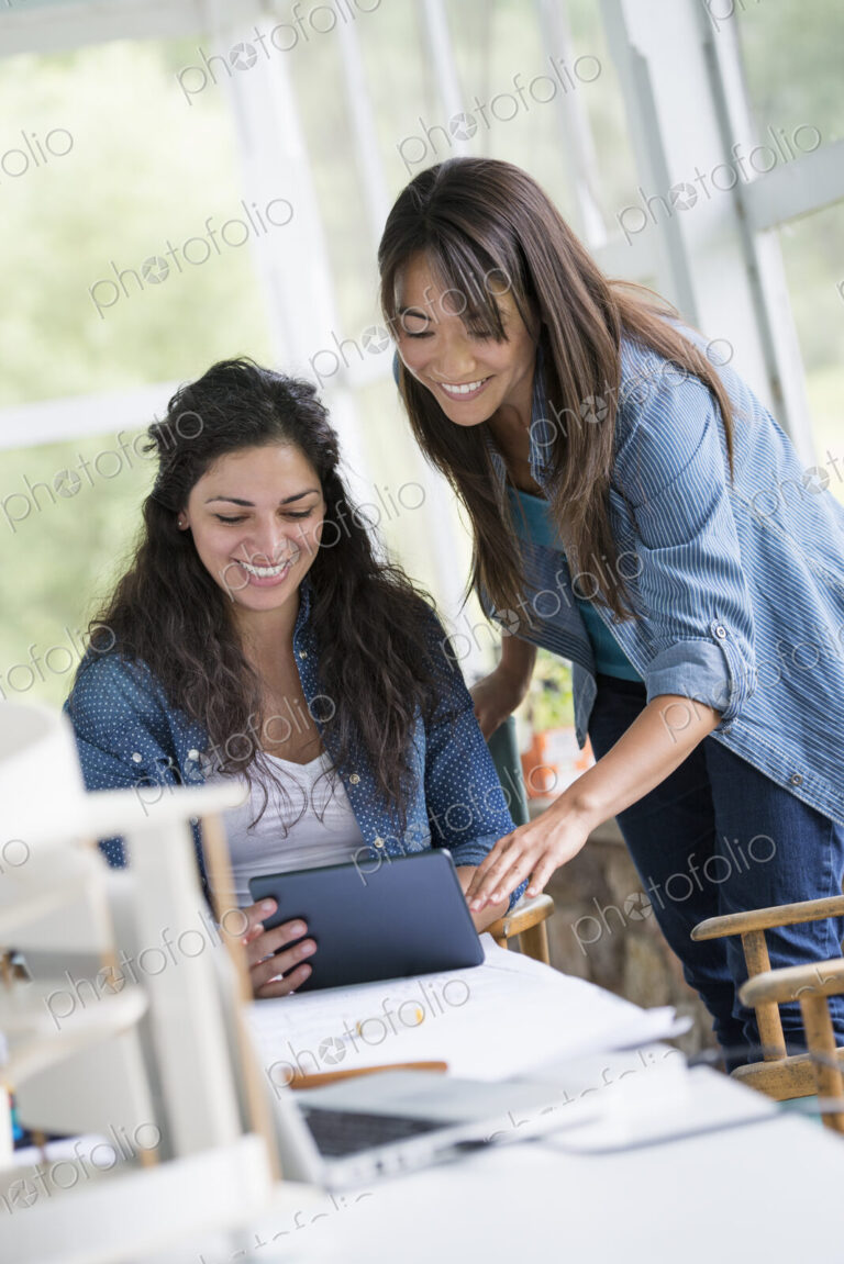 Two women working together, looking at the screen of a digital tablet.
